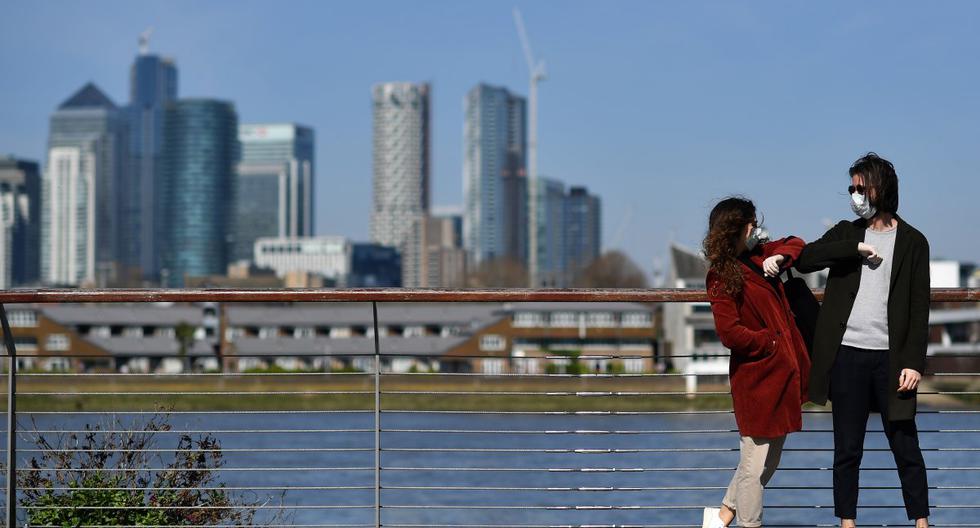 Imagen referencial. Personas con mascarillas se saludan con el codo en Greenwich, en el sur de Londres. (Ben STANSALL / AFP).
