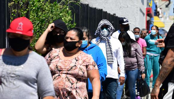 Las personas usan sus máscaras faciales esperando en línea para una distribución de alimentos de emergencia tras haber sufrido la crisis por el coronavirus (Foto referencial: Frederic J. BROWN / AFP)