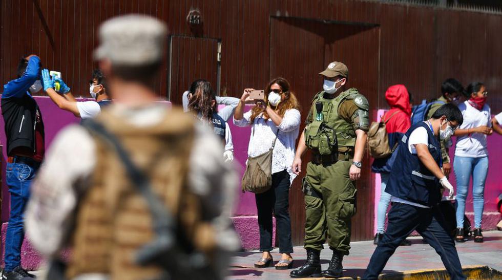Chilean soldiers guard as a Health worker checks the temperature of a Peruvian queuing for a safe-conduct outside the consulate in the Chilean city of Arica, on the border with Peru, on March 23, 2020 while the borders remains closed due to the coronavirus, COVID-19, pandemic. - Chile closed its land, air and sea borders on March 18. (Photo by Patricio BANDA / AFP)